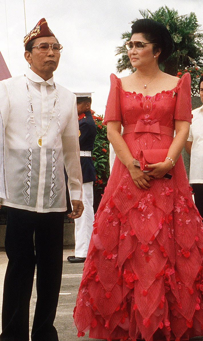 President Ferdinand Marcos and first lady Imelda Marcos of the Philippines dressed in traditional Filipino costumes, 1984. Marcos wears a white shirt with elaborate embroidery and black pants, and Imelda wears a formal red gown with embroidery and high pointed 'butterfly' sleeves.