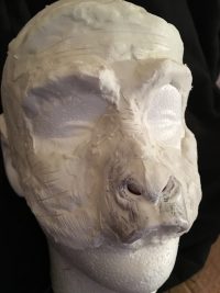 Clay bust of a human head with an animal-like muzzle.