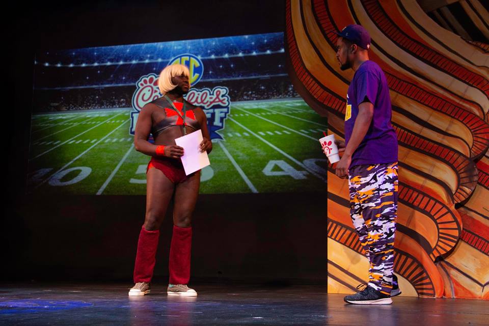 Production photo showing Marcus, cosplaying He-Man at Dragon Con, awkwardly encountering a Black LSU Football Fan attending the Chick-fil-A Kickoff Game.
