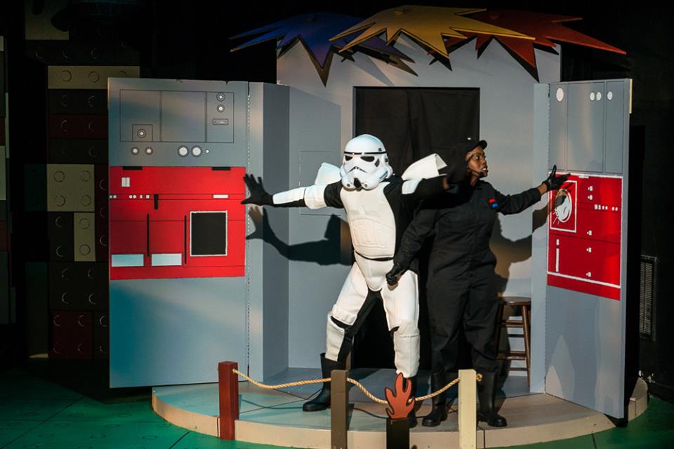 Production photo showing an Imperial Stormtrooper, arms spread, physically upstaging the Ensign as she tries to sing.