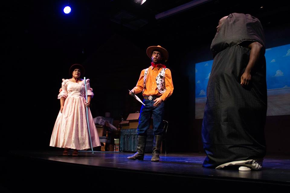 Production photo showing Bo Peep and Sherriff Woody from the Toy Story franchise, with Marcus playing the role of a black dildo.