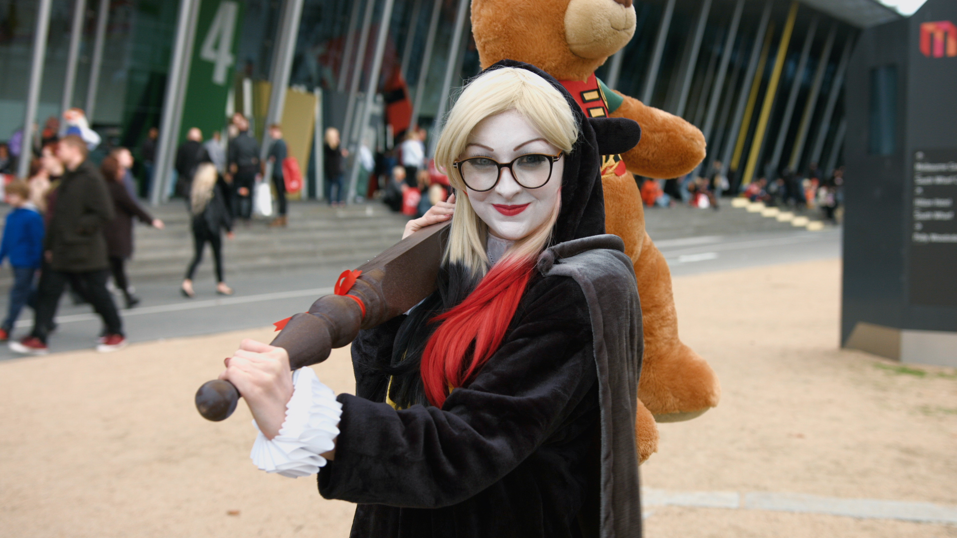Harley Quinn cosplayer wearing a black bear onesie wielding a table leg bearing a stuffed bear dressed as Robin.