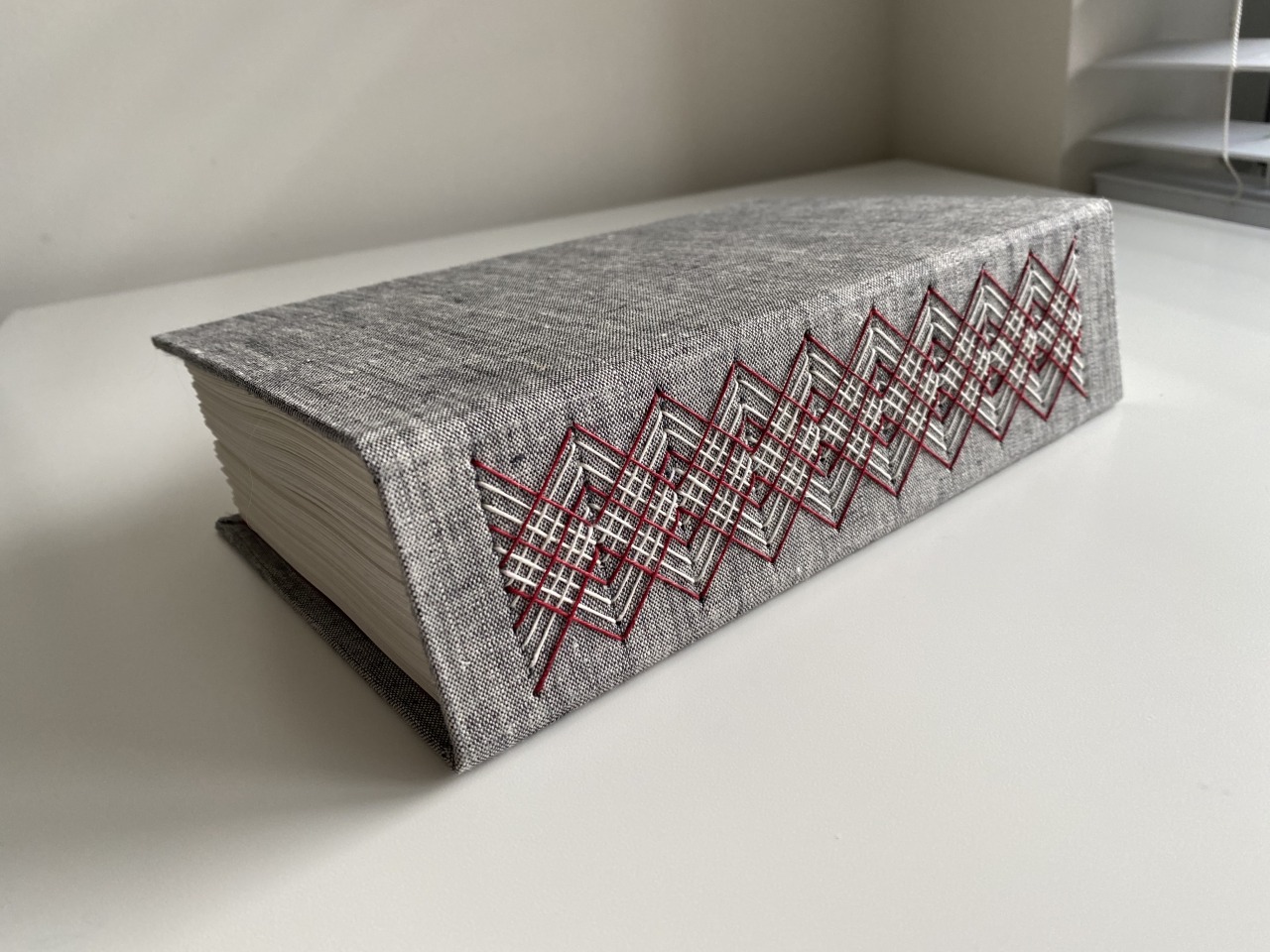 Side-lying hardcover book with ornate red-and-white stitching decorating spine