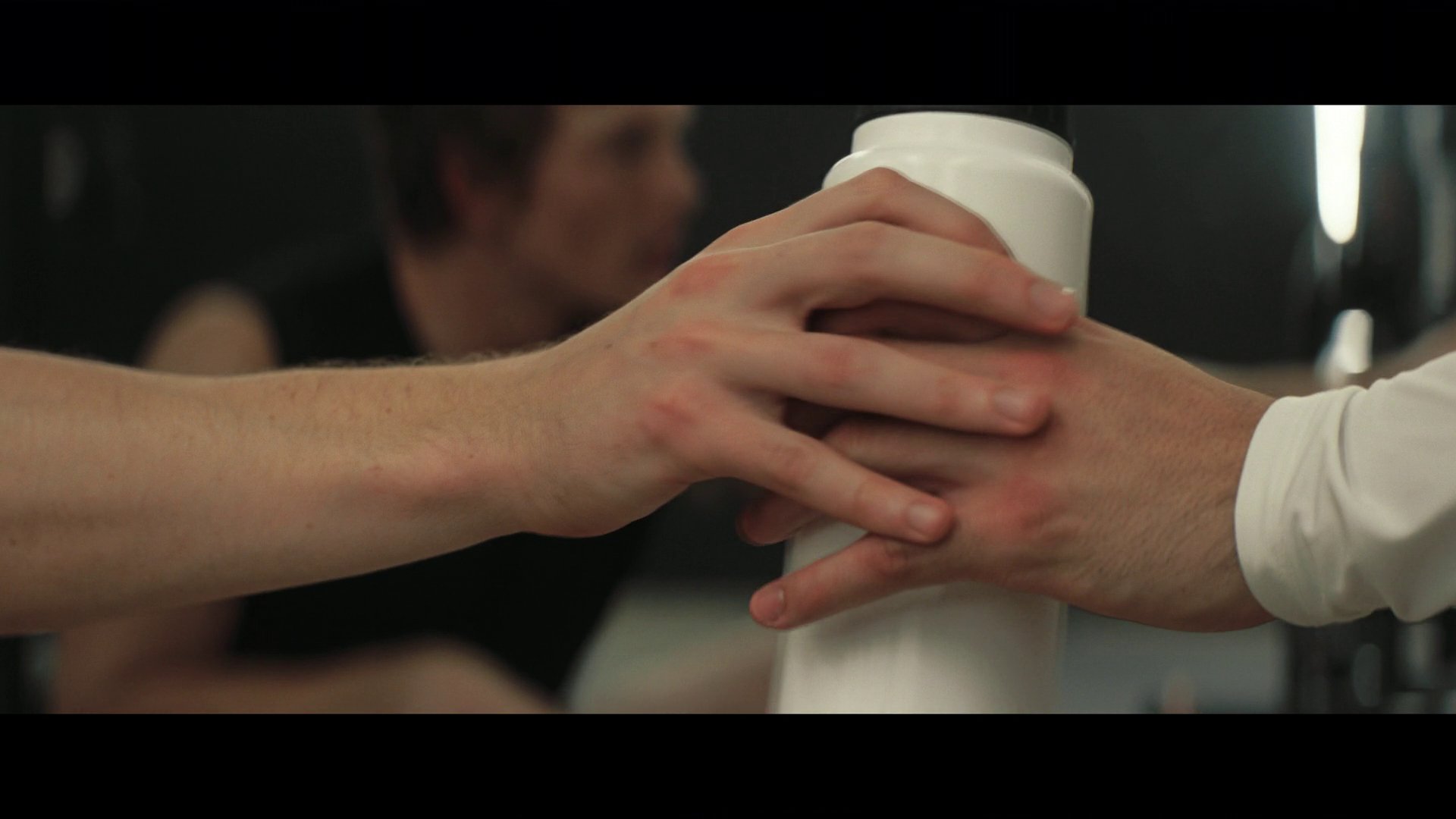 A screenshot that shows a close-up of two hands overlapping and touching while holding a water bottle. Only the hands and bottle are in focus.