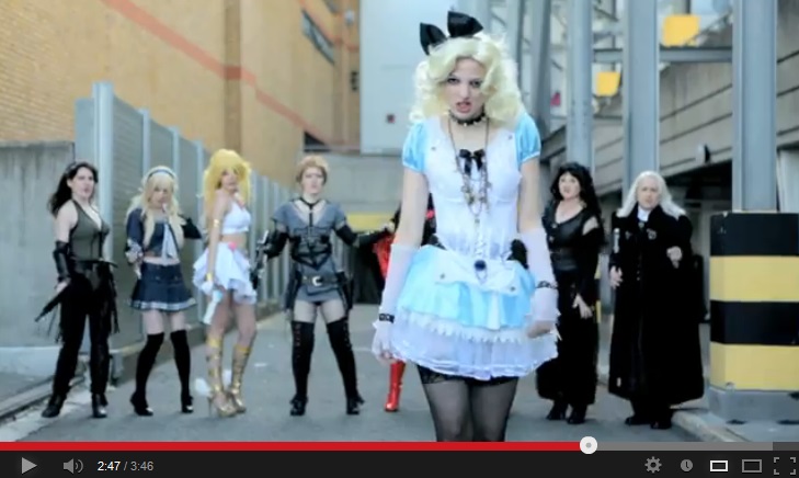 Color image of a sexy blonde woman (Alice) with a big black bow in her hair, standing in the foreground wearing a blue-and-white short dress and black thigh-high semisheer stockings. Behind her is a row of women dressed in various cosplay costumes.