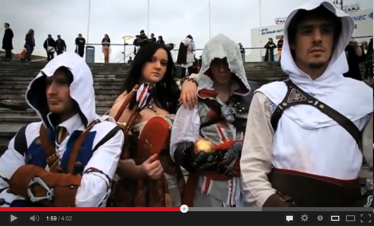 Color image of four people in costume, a bare-headed woman and three hooded men, three of them staring straight at the camera.